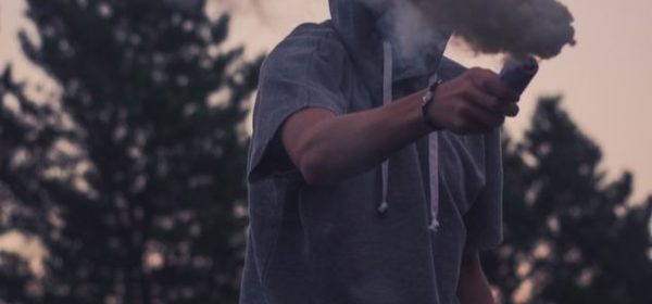 Un jeune homme avec un vêtement à capuchon, tenant un fumigène.